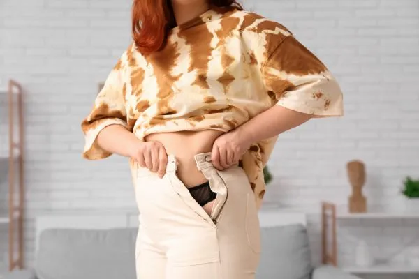 Image of woman trying to do her trousers up after pregnancy weight gain Warfield