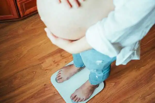 Image of woman weighing herself and experiencing weight gain through pregnancy Warfield